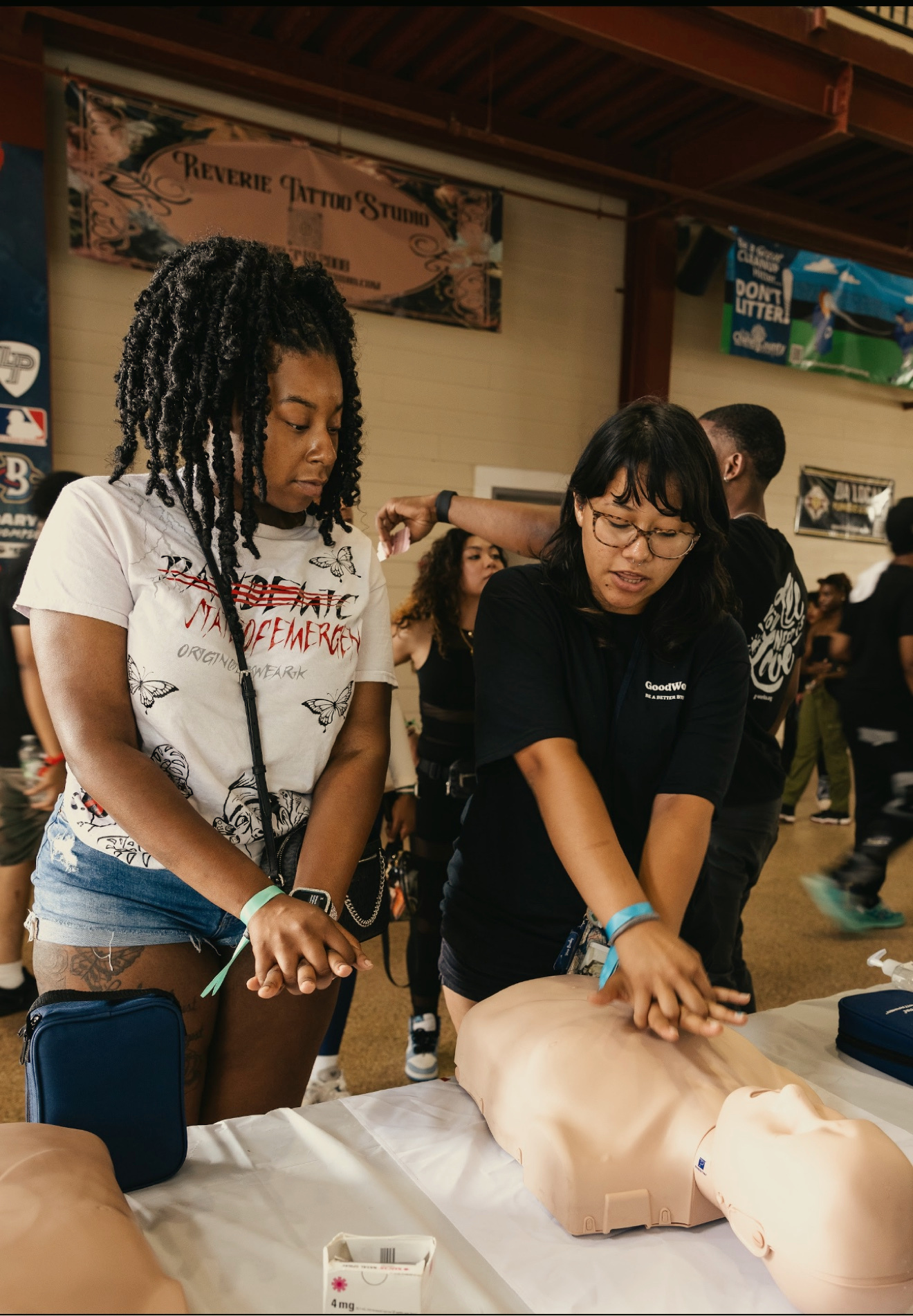 A GoodWorks volunteer teaches CPR compressions on a manikin at a festival booth