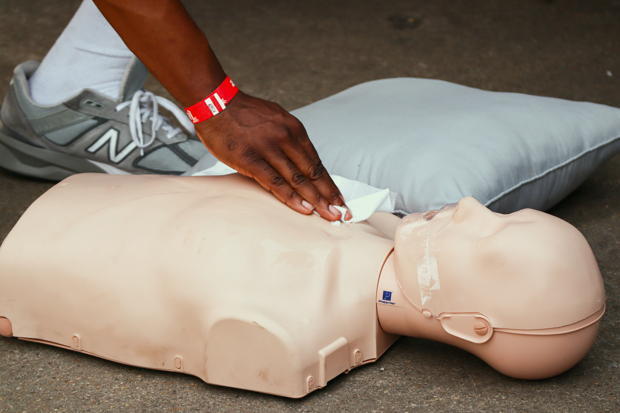 Hands practice chest compressions on a CPR manikin at the GoodWorks DMV SummerJam booth