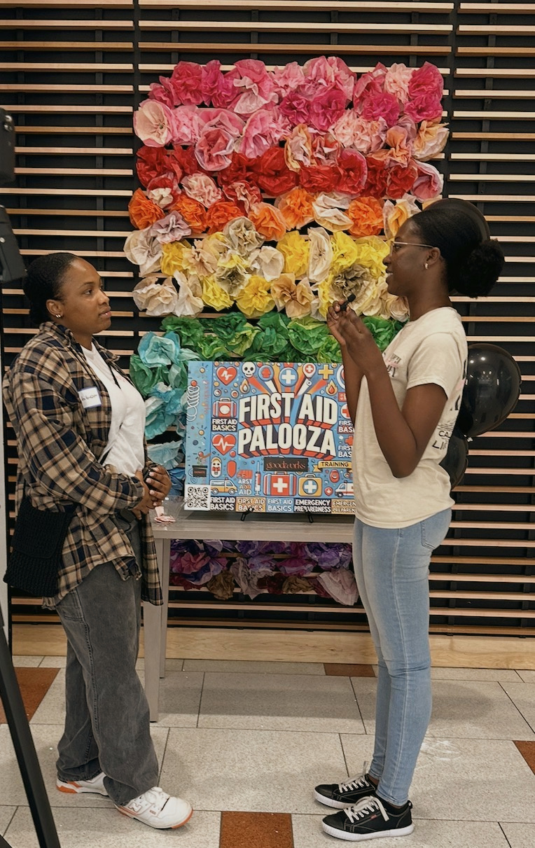 Two attendees talk beside the First Aid Palooza flower wall