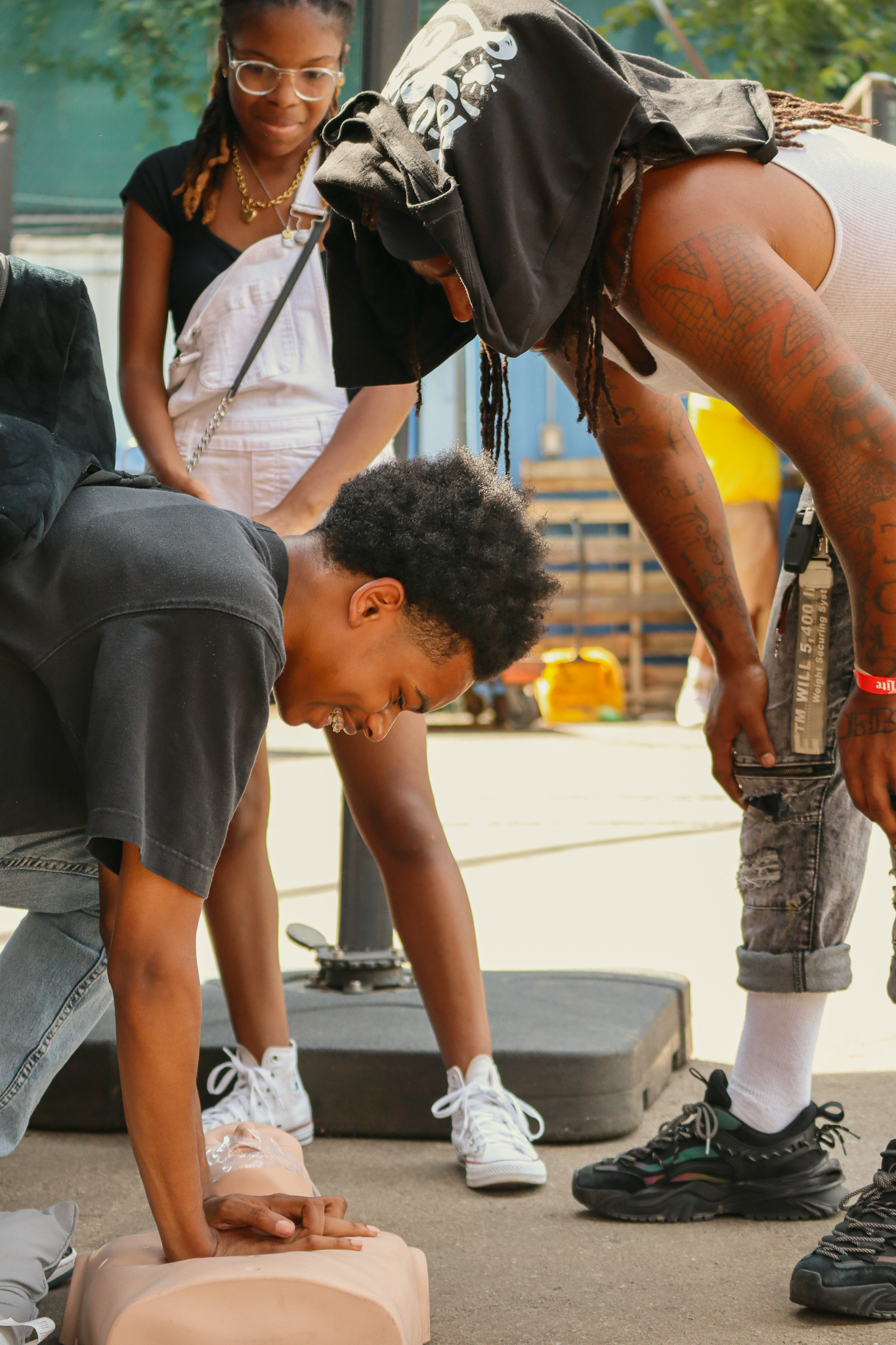 A young man practices CPR compressions on a manikin while a GoodWorks volunteer coaches him at DMV SummerJam